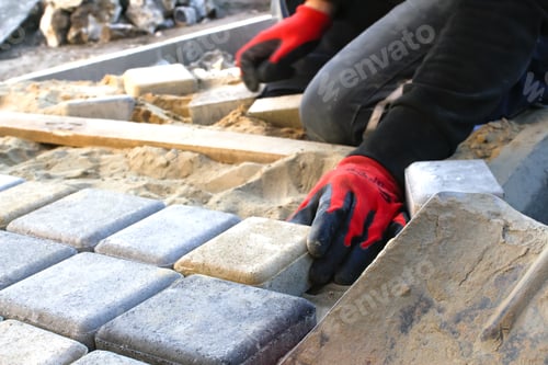 Preview: Paver master in red gloves. Man lays paving stones in layers. Garden brick pathway paving by profess