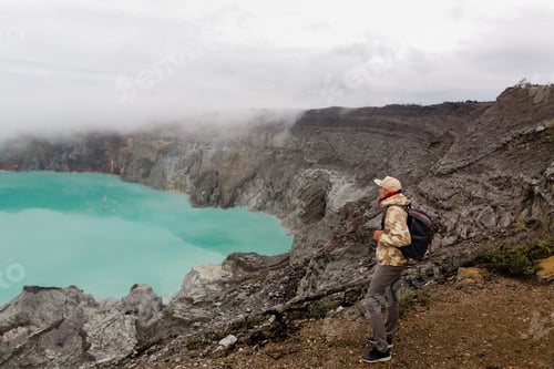 Preview: Man tourist looks at the sulphur lake on the Ijen volcano on the island Java in Indonesia. Hiker man