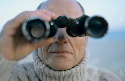 Preview: Man peering through binoculars with focus on the lenses.