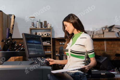 Preview: charming publisher pressing button on panel and holding paper while working in print center