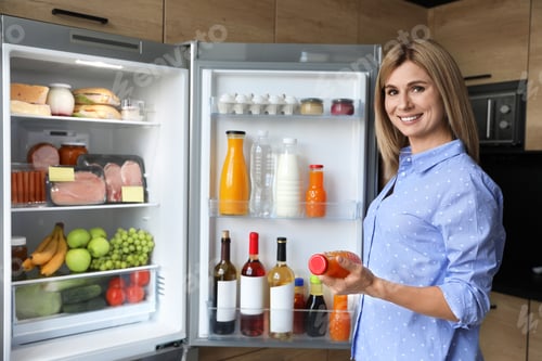 Preview: Woman with bottle of juice near refrigerator in kitchen