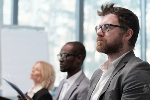 Preview: Young serious bearded businessman looking at speaker during presentation