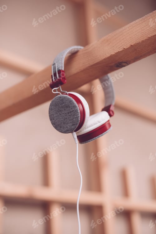 Preview: Modern plastic headphones with cable hanging on wooden beam