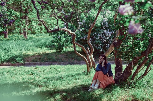 Preview: Teenage girl enjoying a conversation on her smartphone under blossoming lilac trees