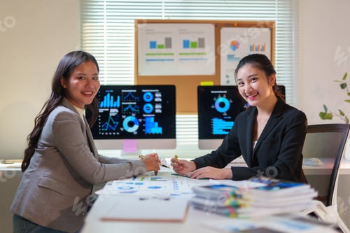 Preview: Asian businesswomen analyzing financial charts on computer in modern office