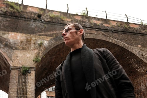 Preview: Stylish man wearing sunglasses posing under brick archway bridge