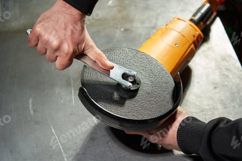 Preview: Hands of a caucasian worker hold an angle grinder and tighten the nut securing the cutting disc
