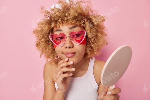 Preview: Beauty day concept. Young woman looks attentively at mirror applies hydrogel patches under eyes unde