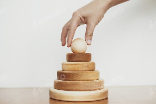 Preview: Eco friendly plastic free modern toys for toddler. Hand holding natural wooden pyramid ring on table