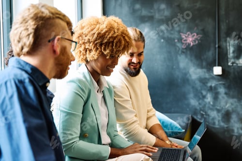 Preview: Multi-ethnic coworkers using laptop together sitting on a comfortable sofa