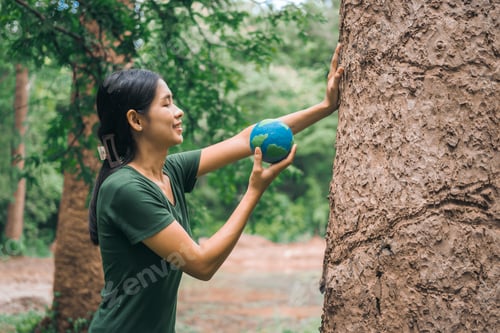 Preview: An Asian woman holds a globe in green forest,symbolizing importance preserving nature.emphasizes