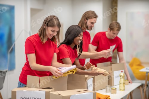 Preview: Young peeple in red packing the cardboards with humanitarian help