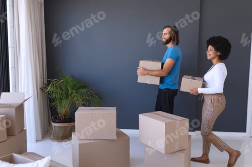 Preview: Happy diverse couple moving house smiling and holding cartons