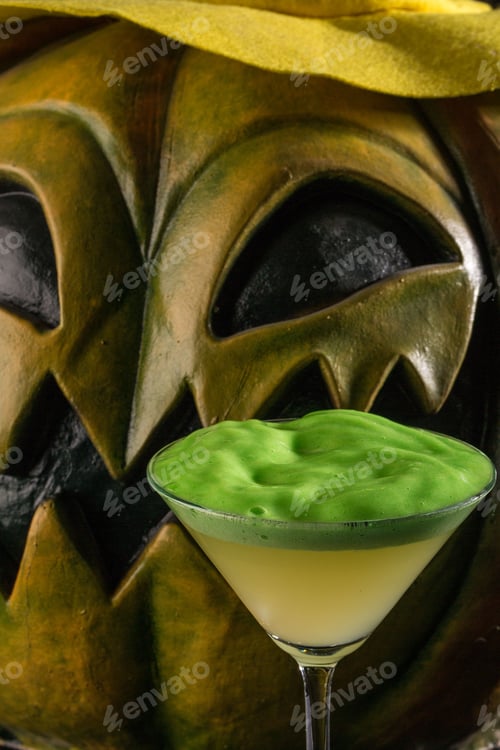 Preview: Vertical closeup of a green cocktail with a foam against a creepy pumpkin mannequin