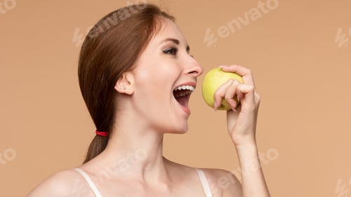 Preview: Beautiful girl with tied on back hair eating tasty apple.