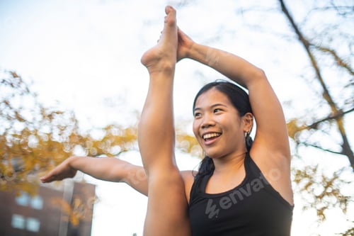Preview: Woman smiling while practicing yoga in an urban park at sunset