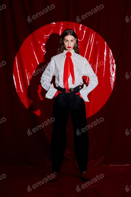 Preview: Captivating young woman posing in stylish attire against a striking red backdrop