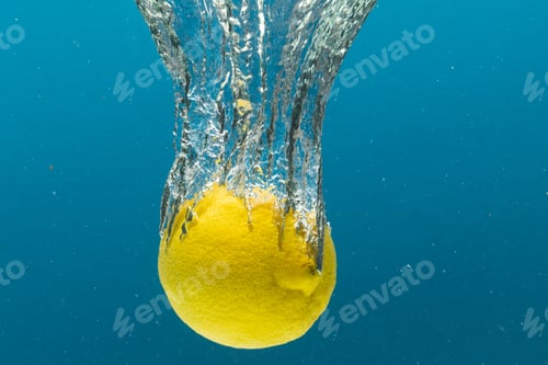 Preview: Close up of lemon falling into water with copy space on blue background