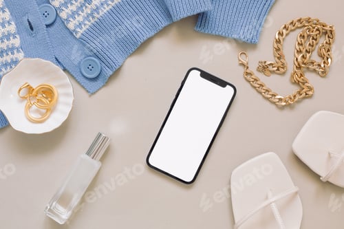 Preview: Top view of blank screen modern mobile phone, female accessories on beige background.