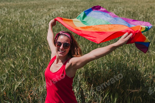 Preview: Woman holding the Gay Rainbow Flag on a green meadow outdoors