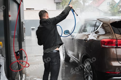 Preview: Young man washing his auto on car wash station.