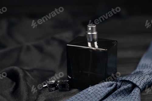Preview: A bottle of mens cologne and cufflinks with blue tie lie on a black luxury fabric background