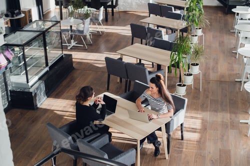 Preview: Two girls in a coffee shop, smiling, gossiping, drinking coffee.
