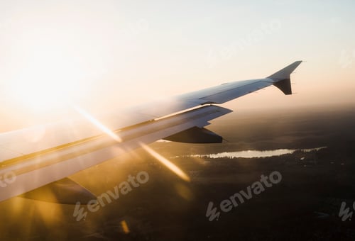 Preview: Elevated view of airplane wing over silhouetted landscape at sunset, Finland