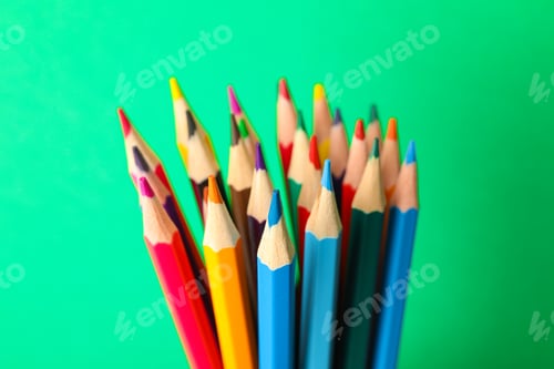 Preview: Multicolored pencils against green background, closeup