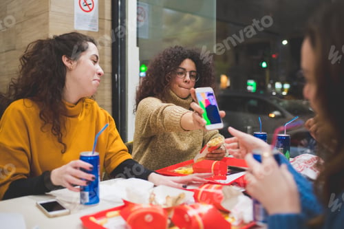Preview: portrait of young women eating together and using smartphone