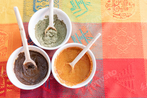 Preview: Three bowls with red, green and yellow mole sauce on top of a colorful traditional tablecloth