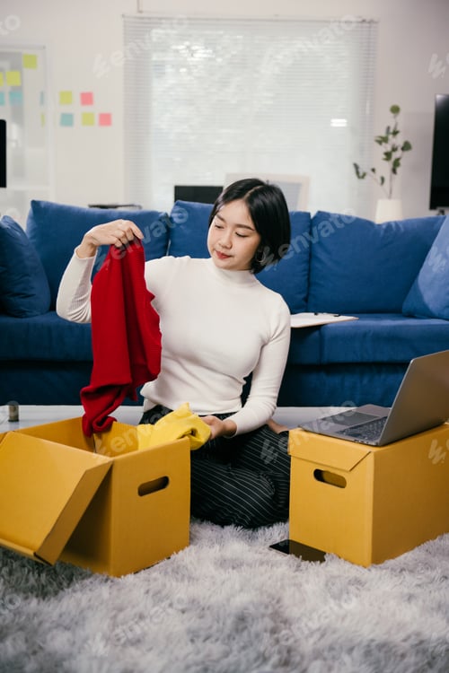 Preview: Asian female entrepreneur preparing clothes shipment from home office