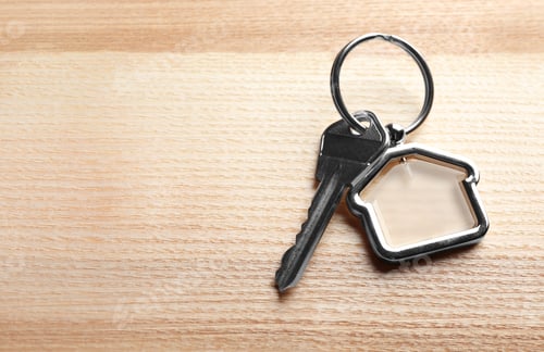 Preview: Key with trinket in shape of house on wooden background. Real estate agent services