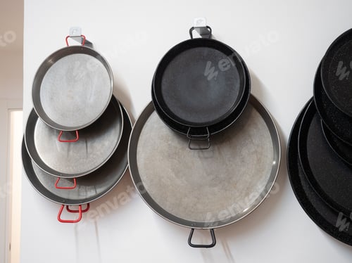 Preview: empty paella pans of different sizes and materials hanging on the wall.