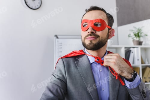 Preview: happy super businessman in mask and cape looking away in office