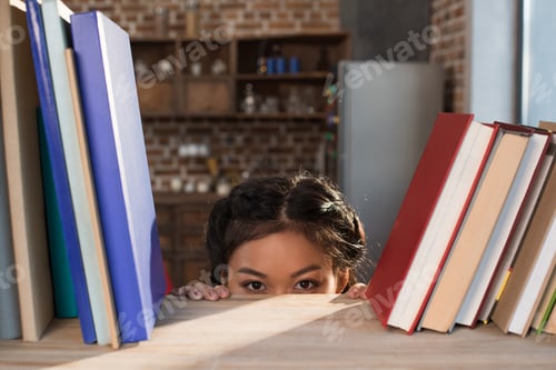 Preview: beautiful smiling asian female student hiding behind bookshelf with books