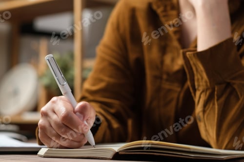Preview: close uop woman hand writing on notebook at worknig desk at home