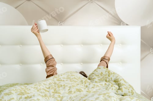 Preview: Young woman waking up in the morning and stretching out her arms up with a cup