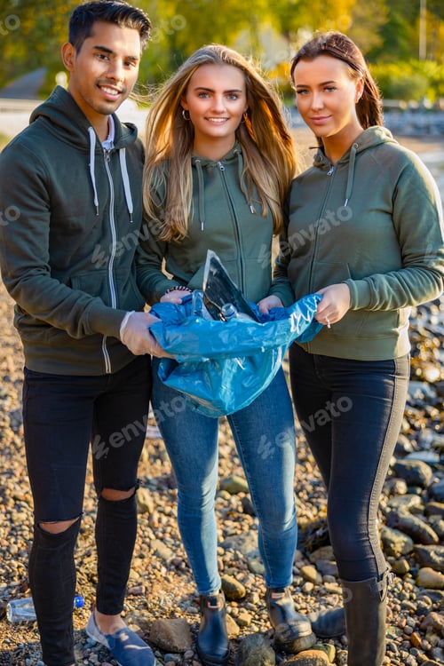 Preview: Smiling team of volunteers holding garbage bag at beach