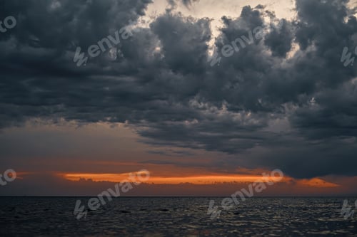 Preview: Beautiful sunset over the sea with gray dramatic clouds and orange sunset streak, dramatic sky