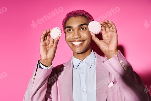 Preview: cheerful man posing with delicious pink zefir near face on pink backdrop, acting like male doll