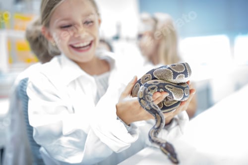 Preview: Happy schoolgirl in science class holding snake