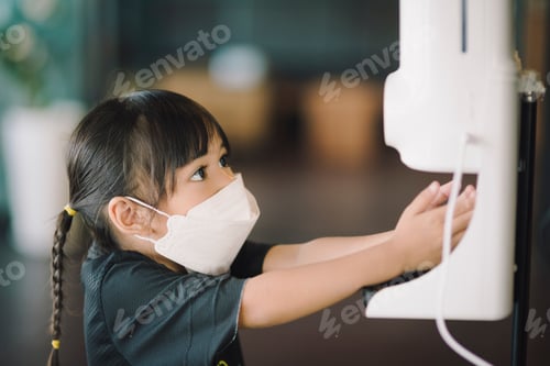 Preview: Little girl wearing mask clean hand with alcohol gel sanitizer auto pump before come to restaurant