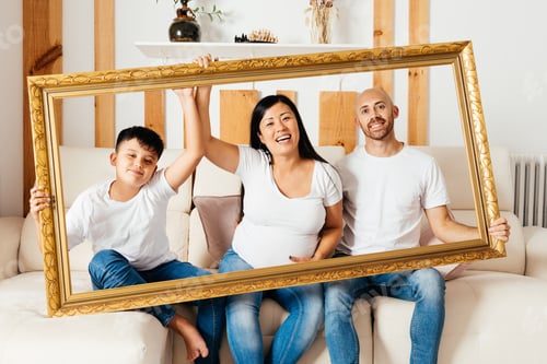 Preview: Eurasian Family Joyfully Posing With a Large Frame in a Cozy Indoor Setting