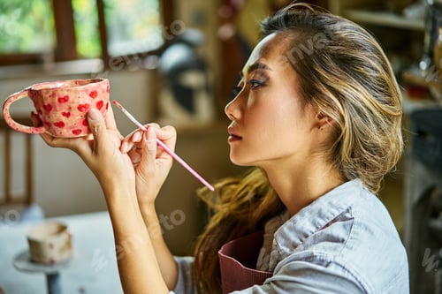 Preview: Female artist decorating and painting handmade ceramic clay cup at her creative workshop