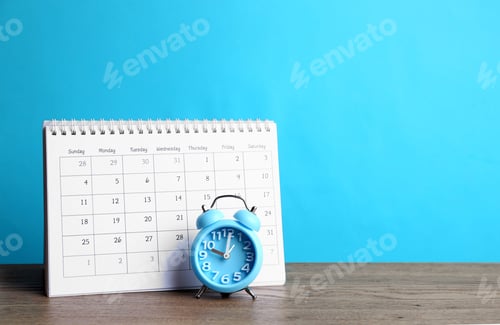 Preview: Calendar and alarm clock on wooden table against light blue background. Space for text