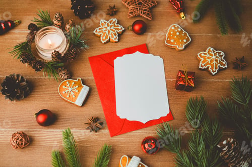 Preview: Christmas greeting card with candle, cookies, pine cones and red envelope on wood