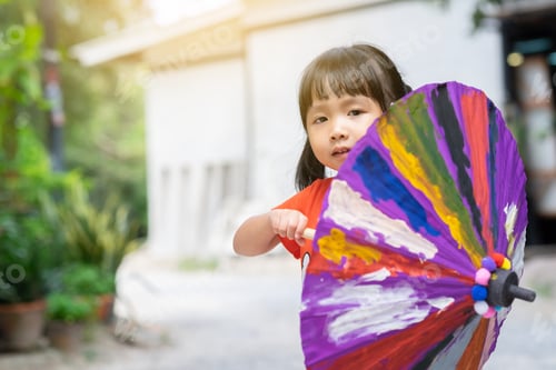 Preview: Upper section portrait of a Thai little girl showing her cute face behind a umbrella she painted