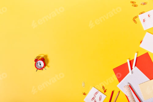 Preview: In center of exposition of school stationery is red small alarm clock.