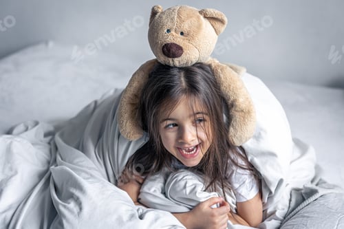Preview: Little cute girl in bed with a teddy bear early in the morning.